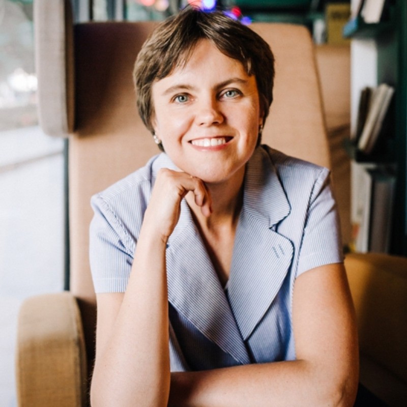 Uśmiechnięta kobieta z podpartą ręką brodą w szarej marynarce